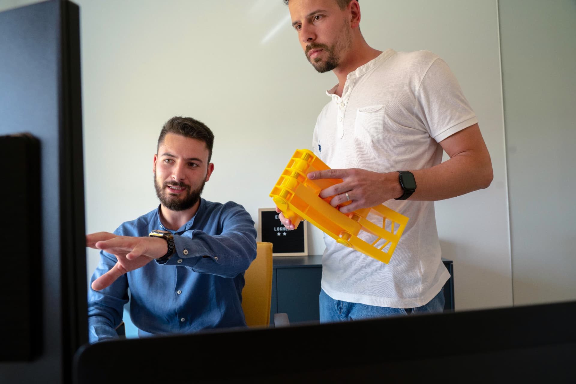 Due tecnici Lokhen Group esaminano un componente stampato in 3D di colore giallo